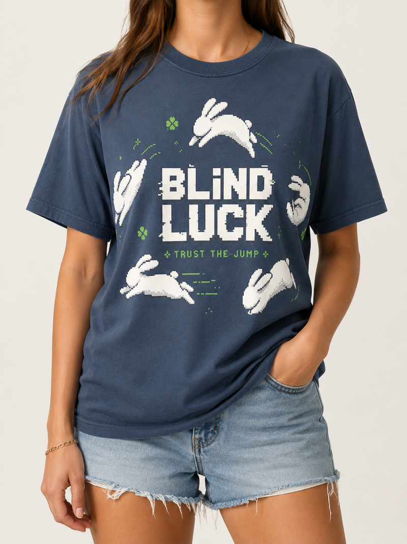 Woman wearing the Ruxel Blind Luck tee in Midnight Navy, front view - pixel-art white rabbits leaping around BLIND LUCK with green four-leaf clovers and Trust the Jump