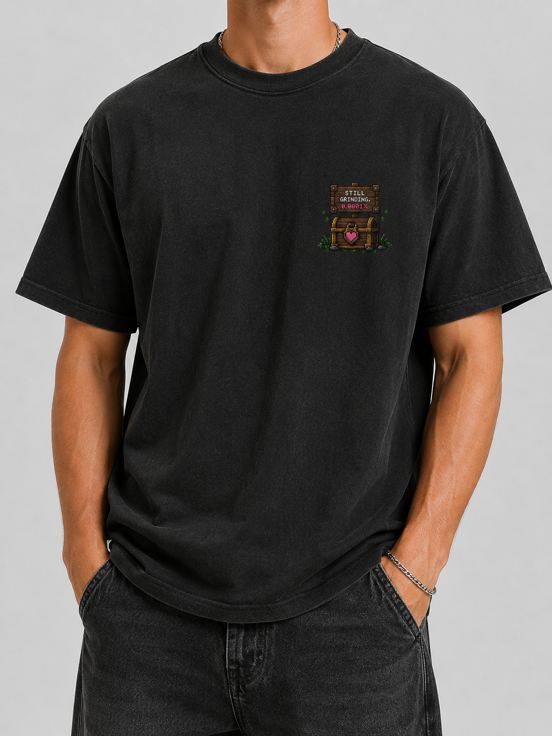 Man wearing the Ruxel Love Drop Rate Vintage Black tee, front view - small pixel Still Grinding sign and heart treasure chest on the left chest