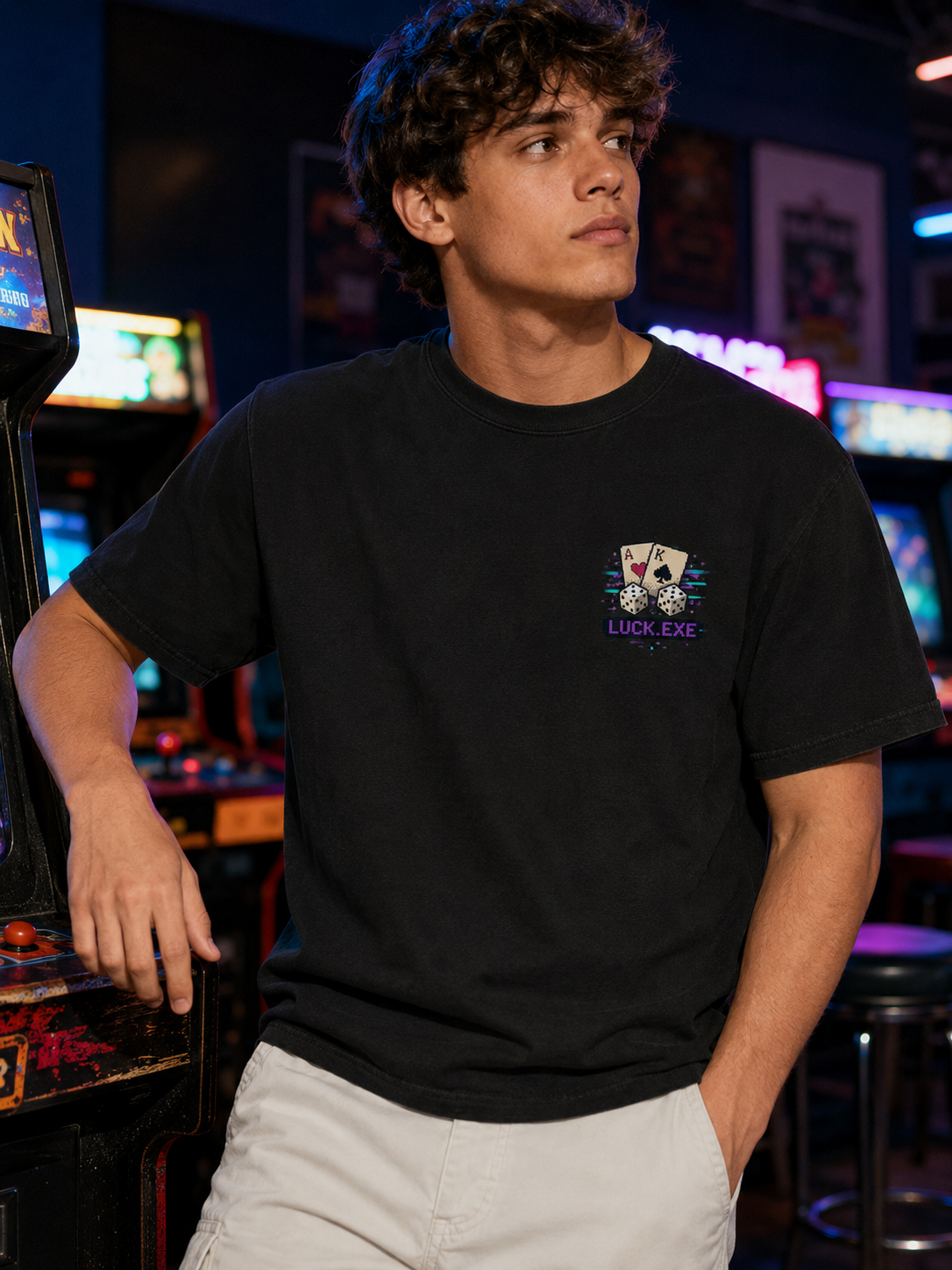 Man in an arcade wearing the Ruxel Luck.exe Vintage Black tee, front view - small pixel-art chest print of playing cards, dice and LUCK.EXE