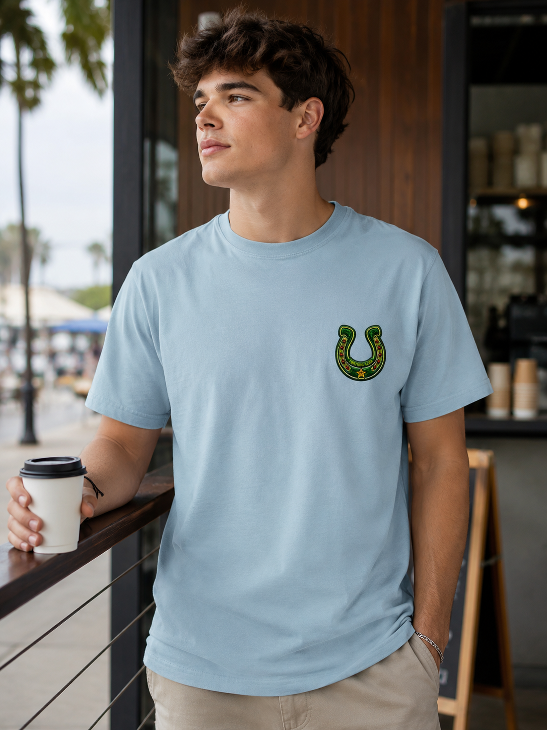 Man wearing the Ruxel Ride the Odds light blue western tee, front view - small green Fortune Club horseshoe crest on the left chest