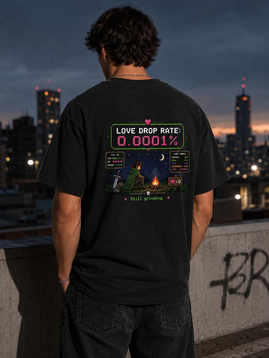 Man on a city rooftop at dusk wearing the Ruxel Love Drop Rate Vintage Black pixel RPG tee, back view showing the loot-screen print
