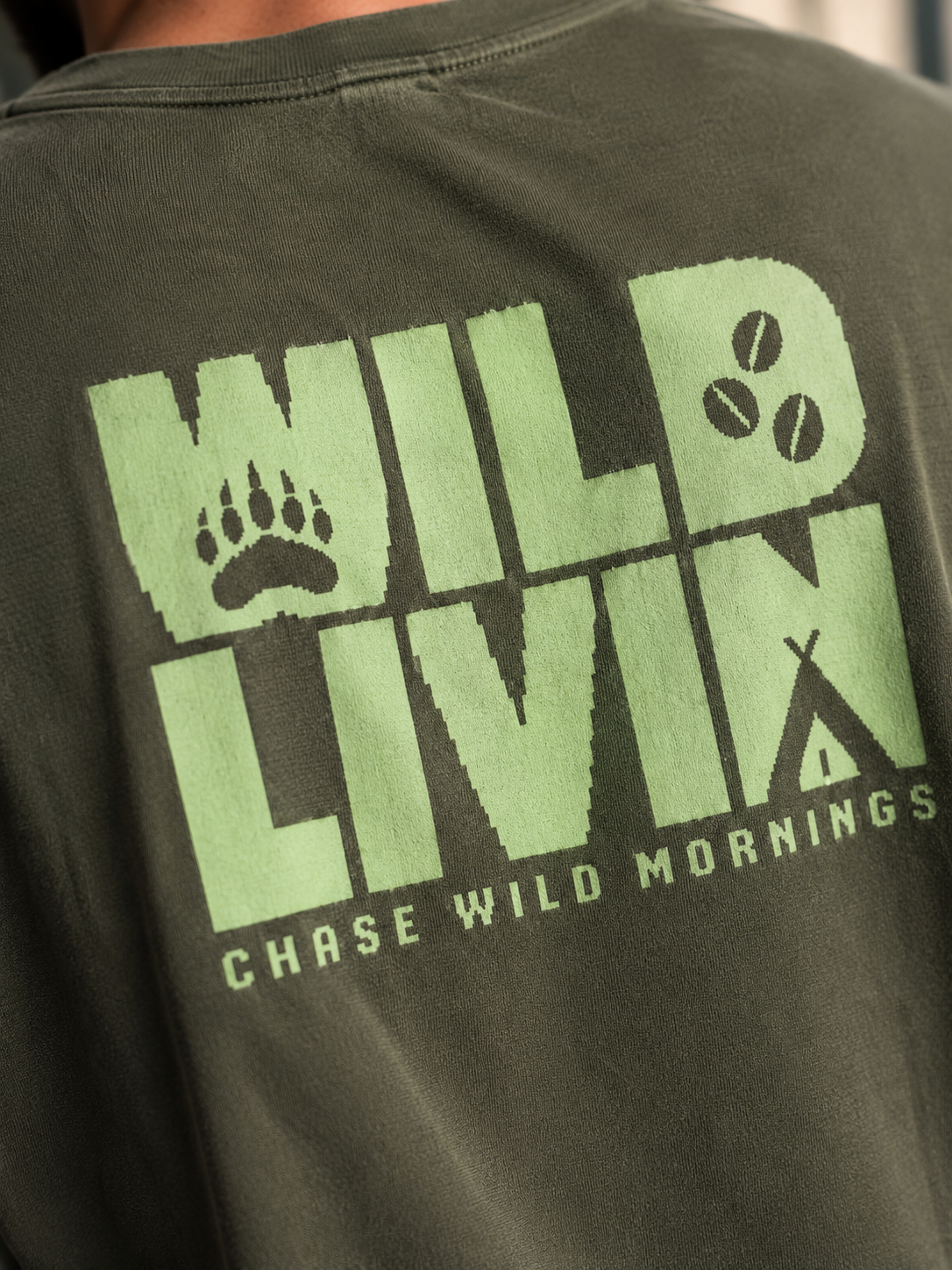 Close-up of the Ruxel Wild Livin back print - pixel bear paw, coffee beans and "Chase Wild Mornings" on olive cotton