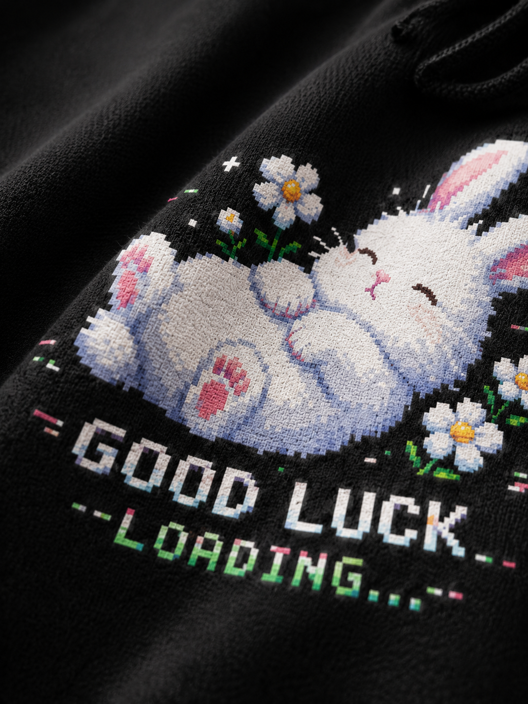 Close-up of the Good Luck Loading pixel print on a Ruxel Void Black hoodie - sleeping white bunny, daisies and GOOD LUCK LOADING text