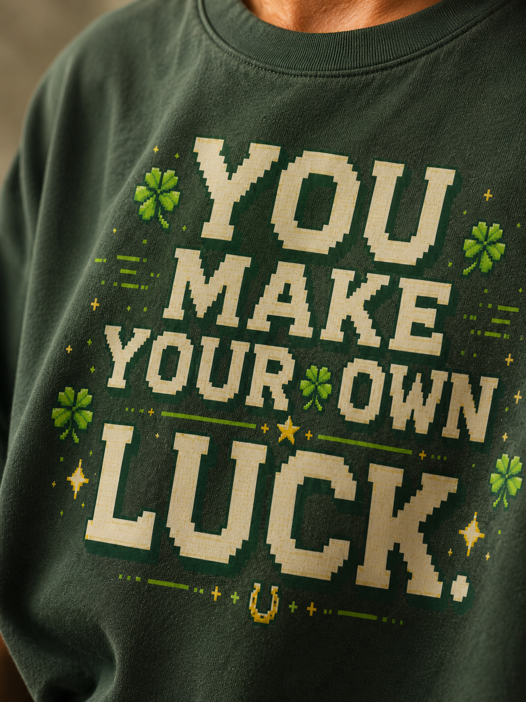 Close-up of the You Make Your Own Luck pixel print on Ruxel Clover Green garment-dyed cotton - cream text, green four-leaf clovers, gold stars and a horseshoe