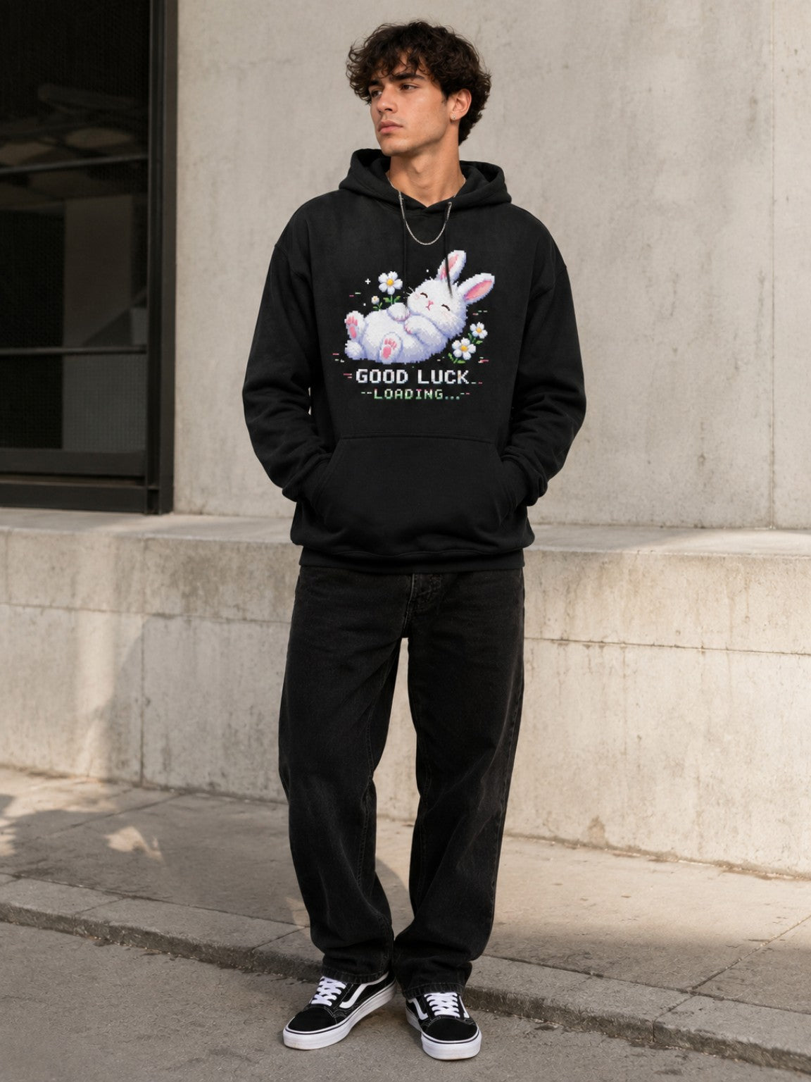 Male model styling the Ruxel Good Luck Loading Void Black pixel bunny hoodie beside modern concrete architecture