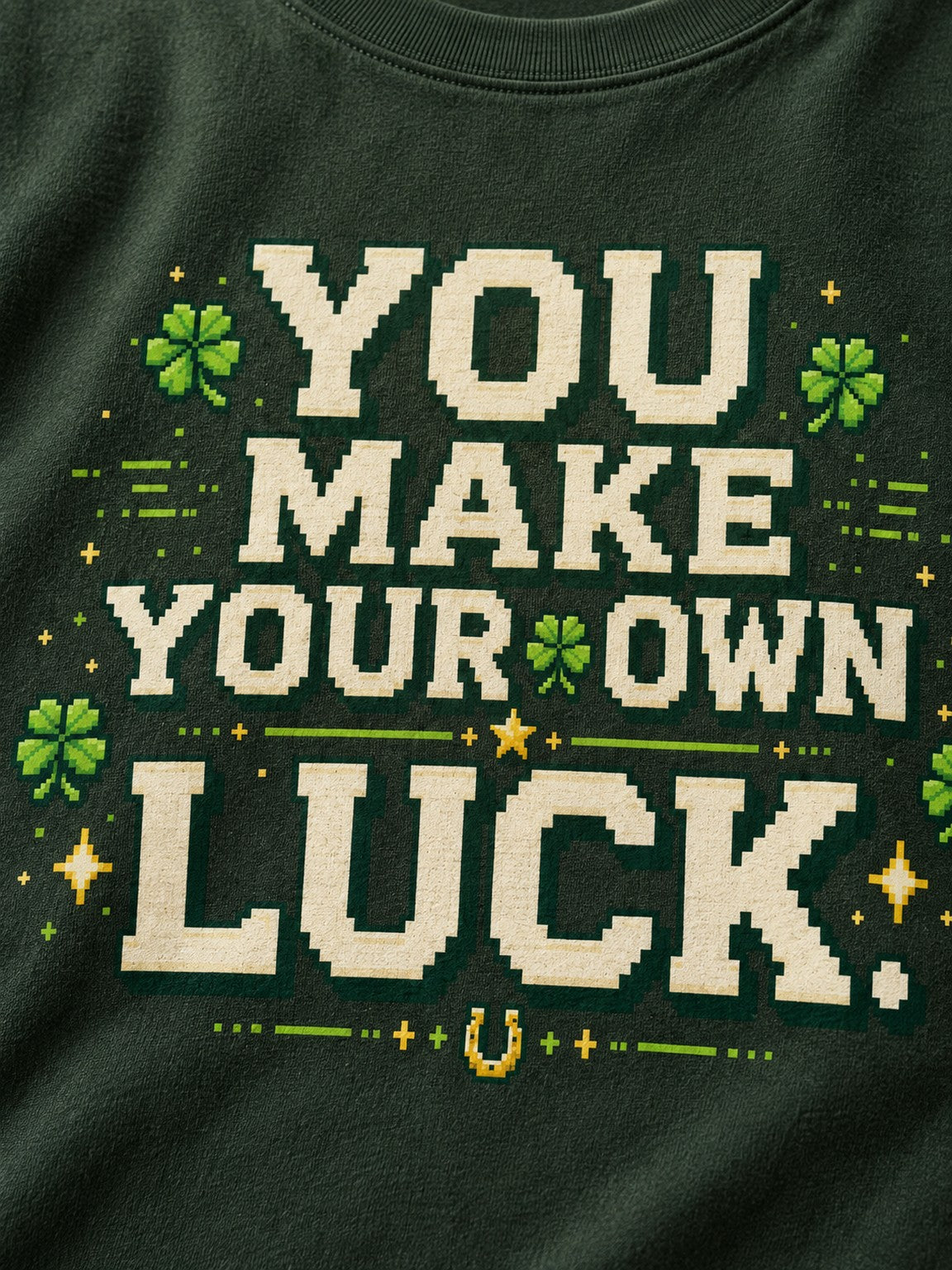 Close-up of the cream You Make Your Own Luck pixel artwork with four-leaf clovers and a horseshoe on the Clover Green tee